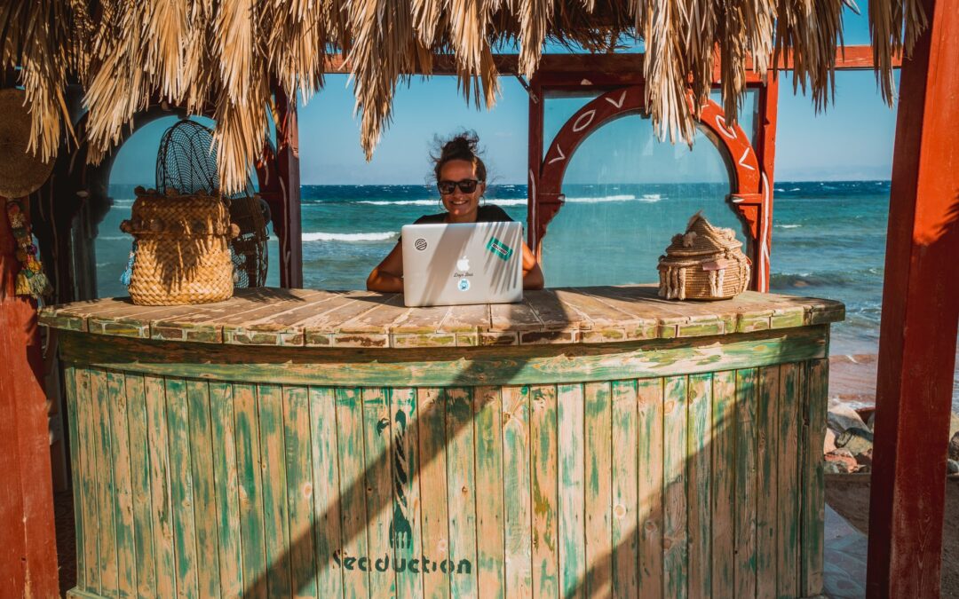 a woman in working remotely in an exotic beach bar with the sea in the background