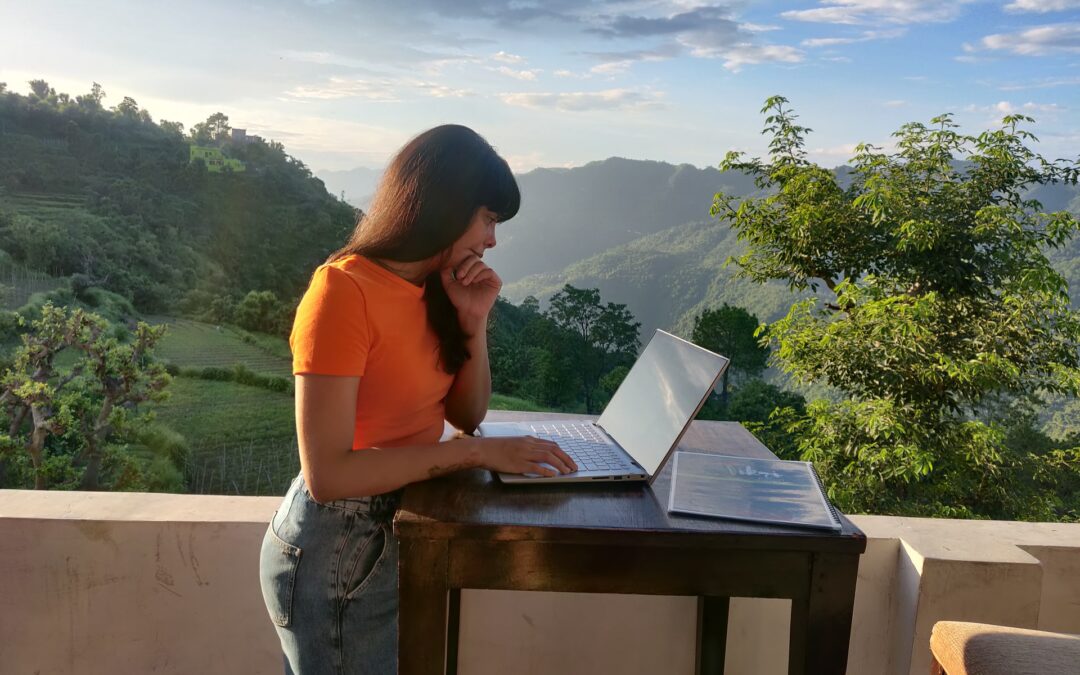 A woman with long brown hair is standing at a remote work desk outside on a terrace